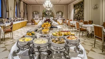 Montaje tipo bufé con diversos alimentos y cubiertos en un comedor formal con candelabros y decoración clásica.