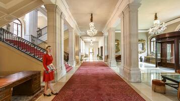 A grand hallway with a red carpet, marble columns, and chandeliers.