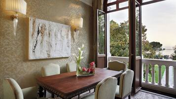 A dining area with a wooden table, six chairs, a vase with flowers, and a large window with a view of greenery and a body of water.