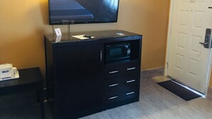 A hotel room with a flat-screen TV mounted on a black cabinet, a microwave, and a door with a security lock. - Travelodge by Wyndham Bay Shore Long Island (Bay Shore)