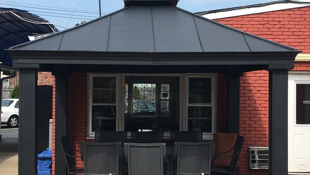 A gazebo-style outdoor seating area with a brick wall backdrop, featuring a table and four chairs. - Travelodge by Wyndham Bay Shore Long Island (Bay Shore)