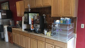 A kitchen with wooden cabinets, a coffee machine, a refrigerator, and a water dispenser. - Travelodge by Wyndham Bay Shore Long Island (Bay Shore)