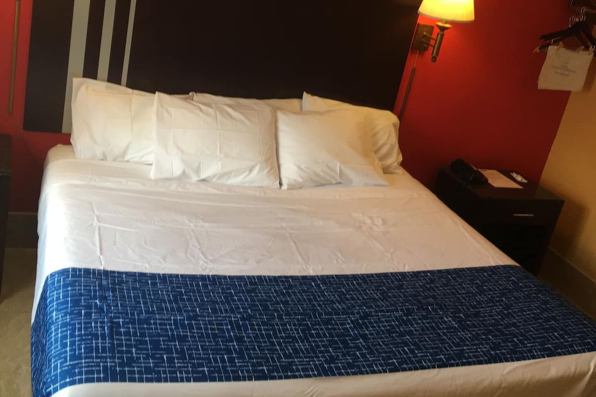 A hotel room with a large bed, two bedside lamps, a red wall, and a black and white striped headboard.