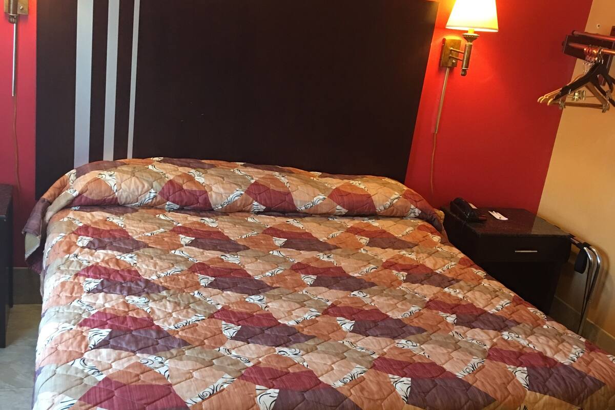 A bed with a quilt, two wall-mounted lamps, and a black headboard.