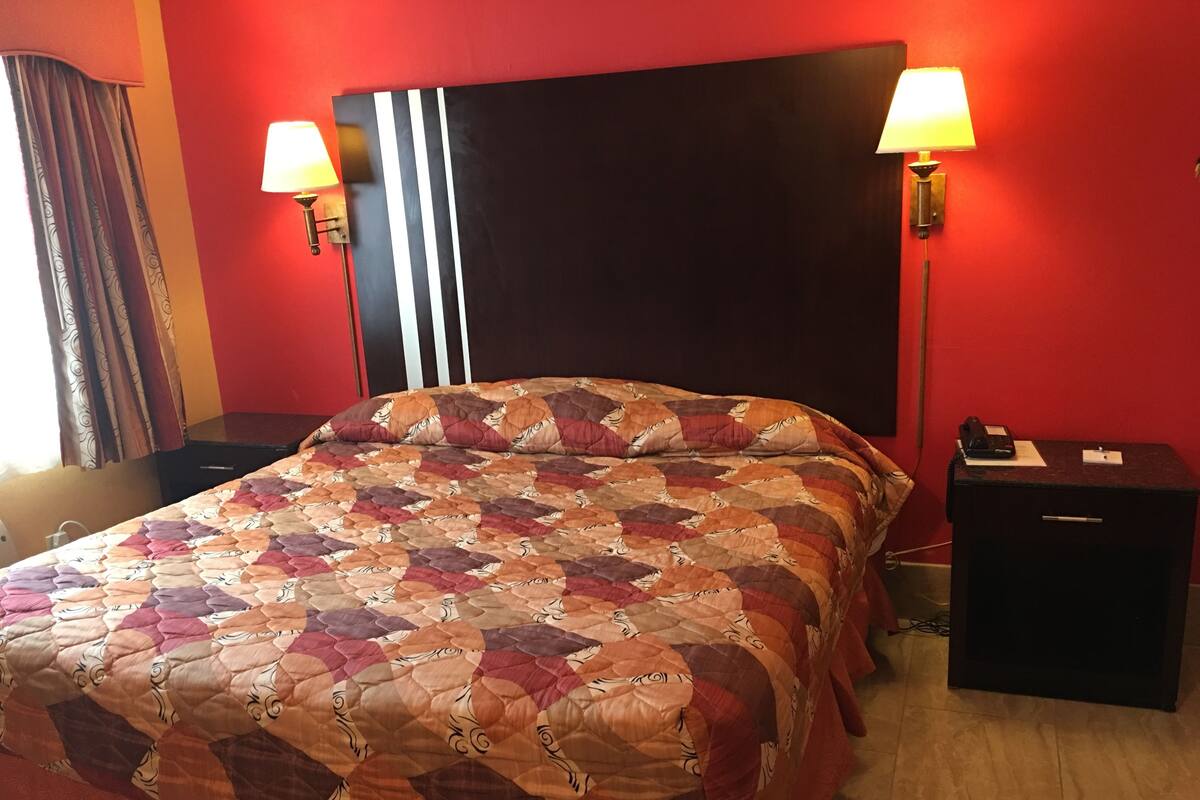 A hotel room with a large bed, two bedside lamps, a nightstand, and a red wall.