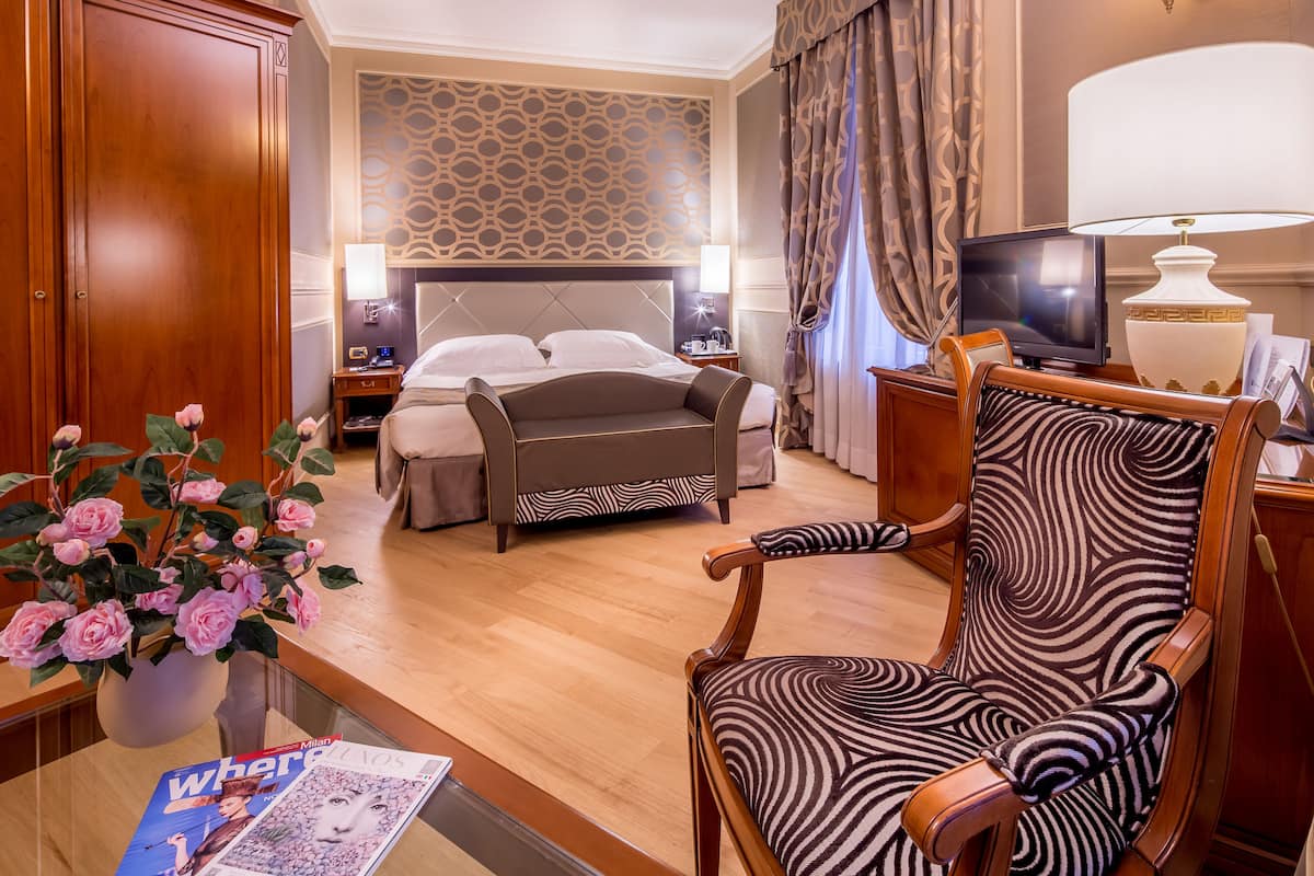 Une chambre d’hôtel comprenant un lit, une télévision, un bureau avec une lampe, une chaise et un vase de fleurs.