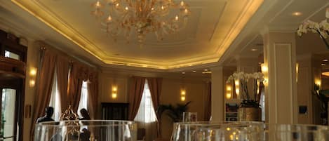 A grand hall with a chandelier, clear glass vases with flowers, and a marble floor.