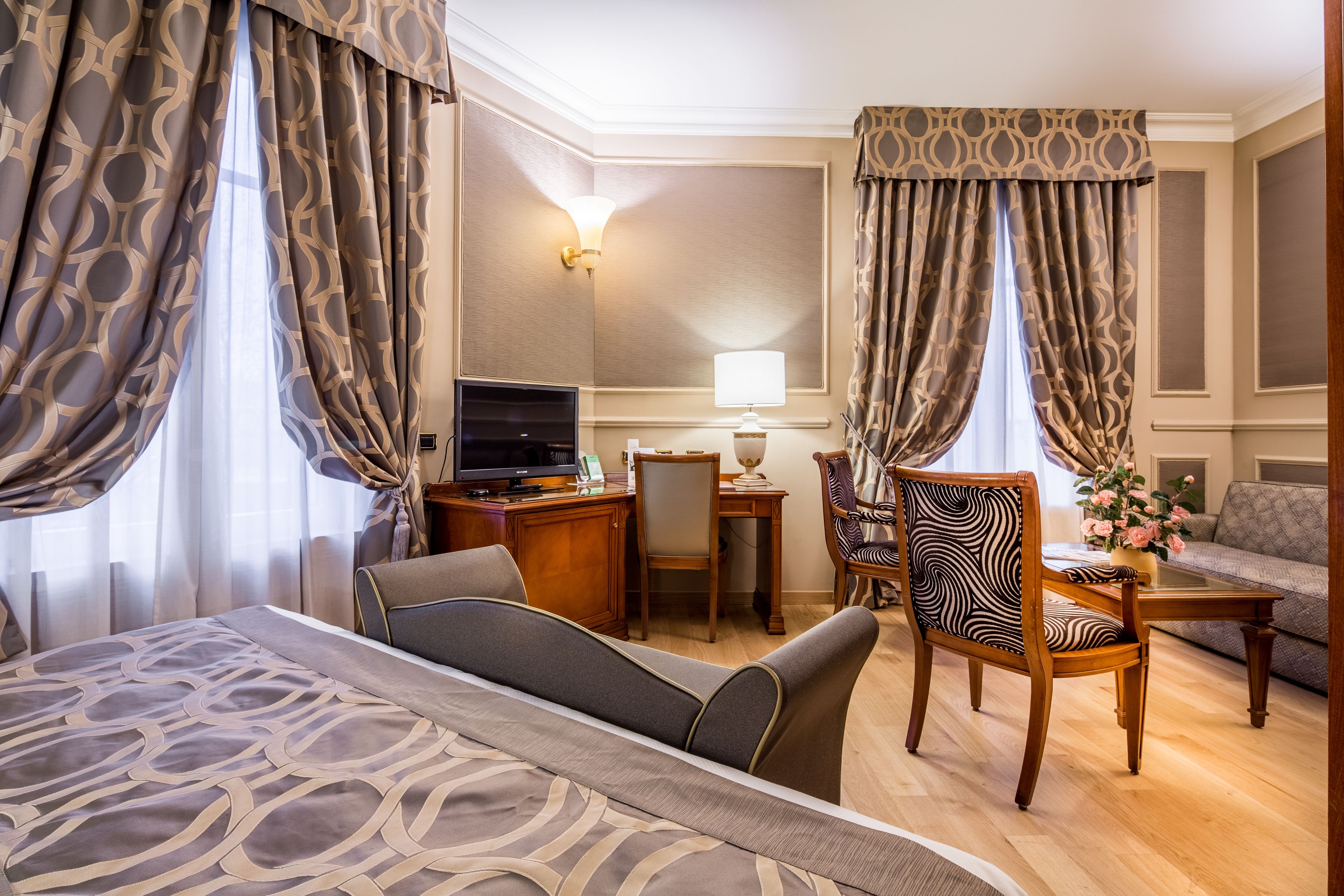 A hotel room with a bed, a desk, a chair, a sofa, and curtains.