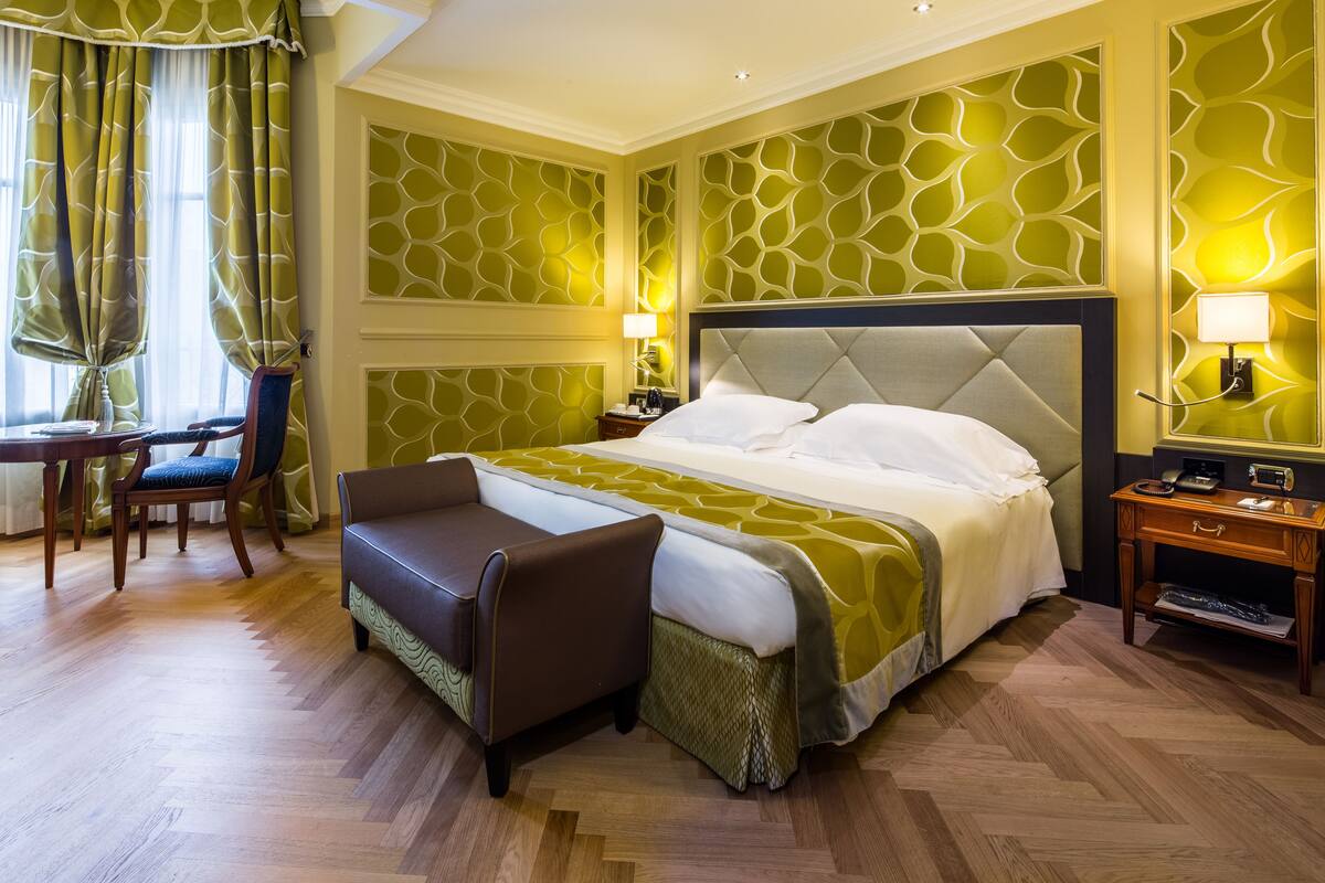 Une chambre d’hôtel avec un grand lit, un coin salon avec un banc, un bureau et une chaise.