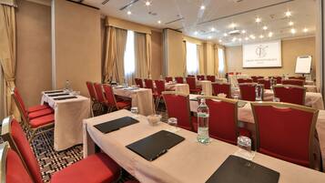Un salón de conferencias con mesas, sillas y una pantalla de proyector mostrando "GRAND VISIT PALACE MILANO".