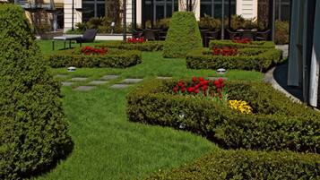 Ein gepflegter Garten mit ordentlich geschnittenen Hecken, verschiedenen Blumen und einem Gebäude im Hintergrund mit klassischer Architektur.
