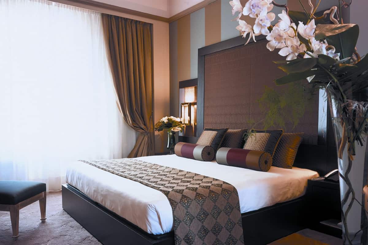 Une chambre d’hôtel moderne avec un grand lit, une table de chevet, un vase de fleurs et une vue sur l’extérieur.