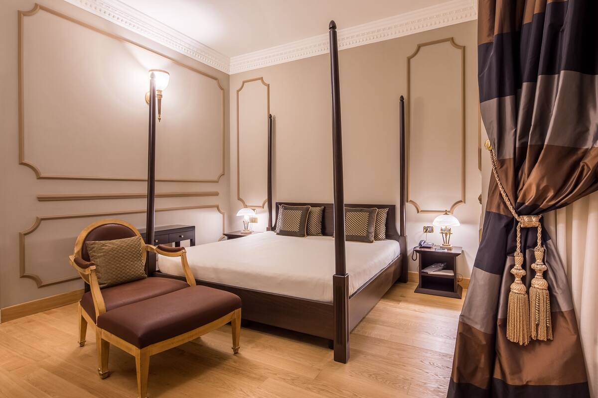 Un lit à baldaquin avec un cadre en bois, une table de chevet avec une lampe et une chaise avec un coussin.