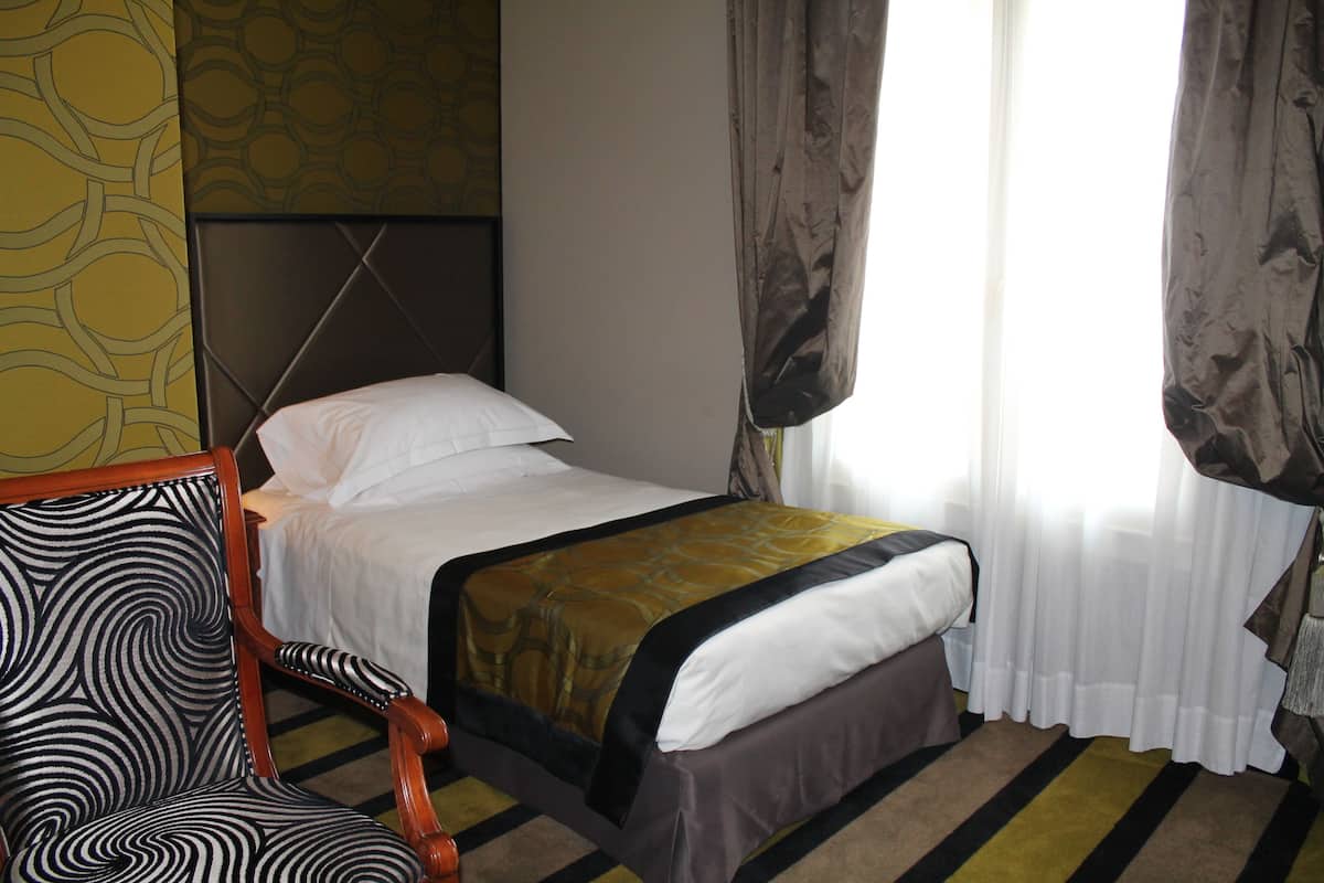 Une chambre d’hôtel avec un lit, une chaise et une fenêtre avec des rideaux.