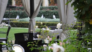 An outdoor seating area with a table, chairs, and a piano. There are curtains and a view of a well-manicured garden with hedges and statues. - Grand Visconti Palace (Milan)