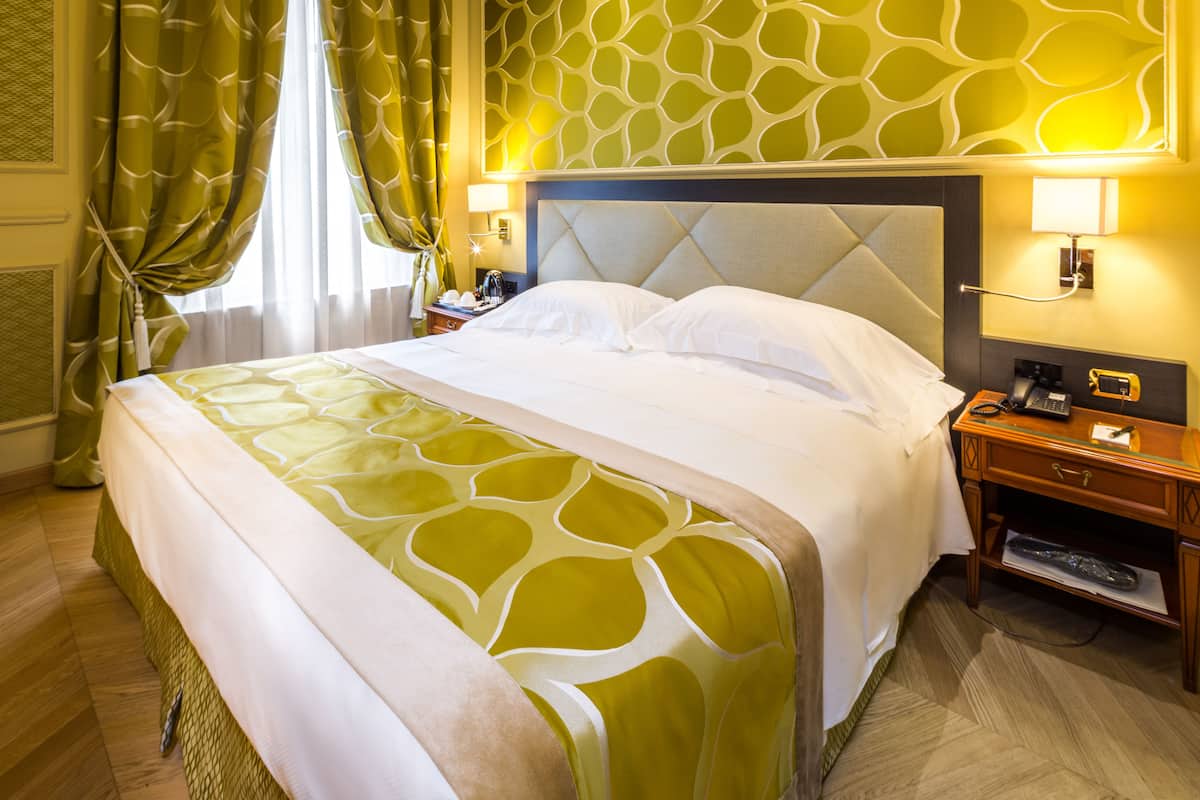 Une chambre d’hôtel avec un grand lit, une table de chevet et une lampe fixée au mur.