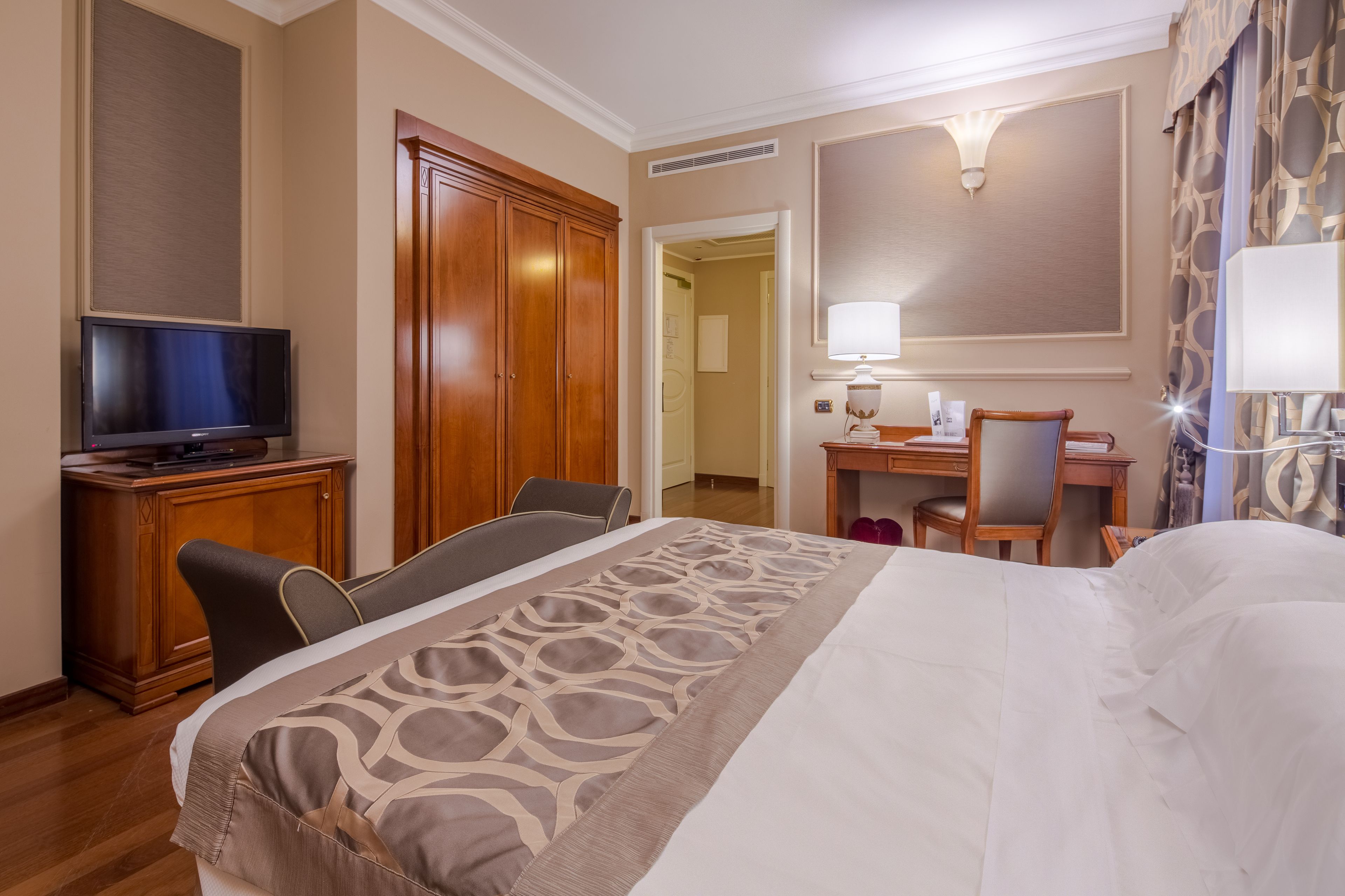 Een hotelkamer met een bed, een bureau, een stoel, een televisie en een garderobe.