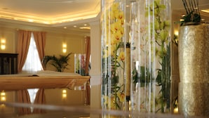 A hotel lobby with a reflective floor, a large transparent vase with yellow flowers, and a textured gold vase. - Grand Visconti Palace (Milan)