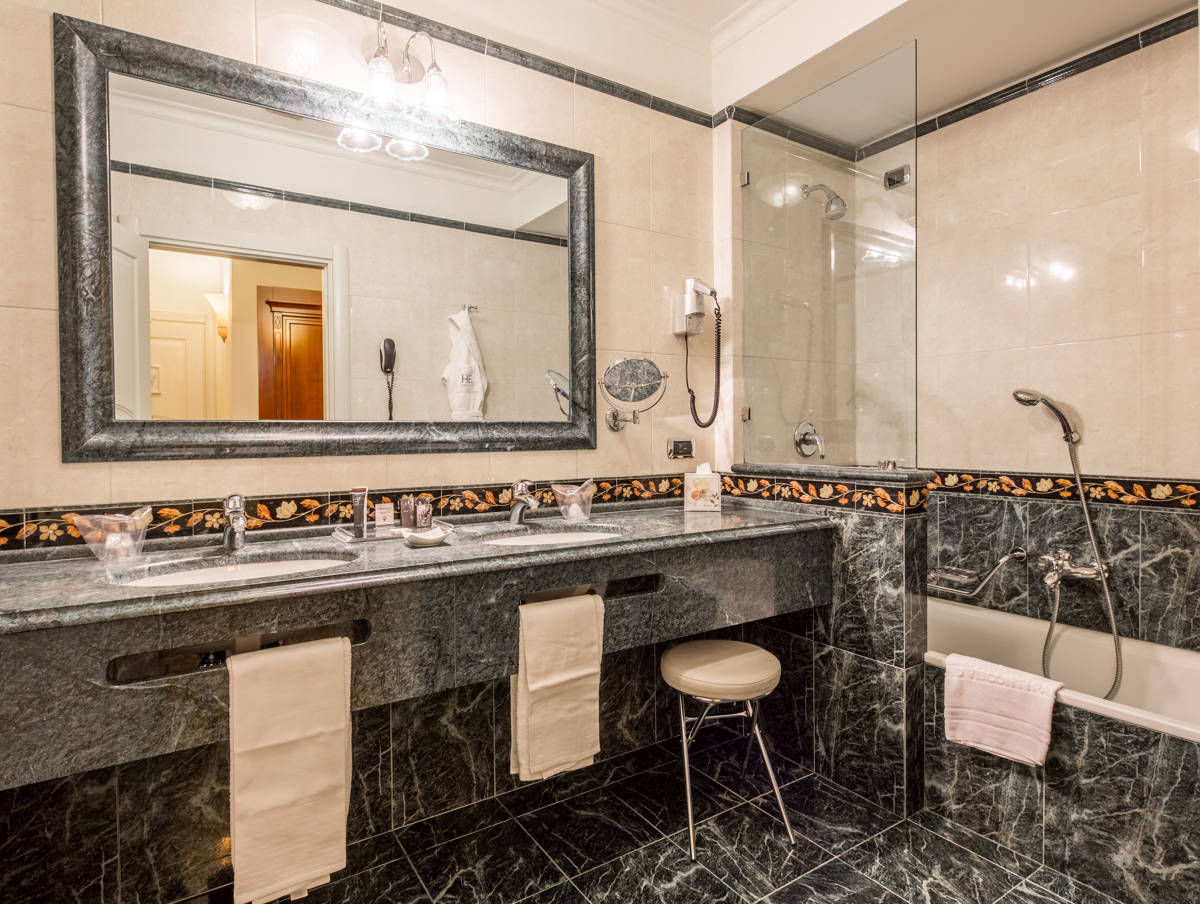 Un baño con tocador de mármol, un espejo grande, ducha e inodoro.