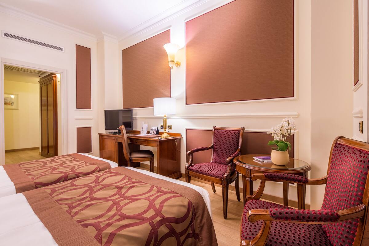 Une chambre d’hôtel avec deux lits, un bureau, une chaise, une petite table et un téléviseur.