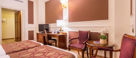 Ett hotellrum med två sängar, ett skrivbord, en stol, ett litet bord och en TV.