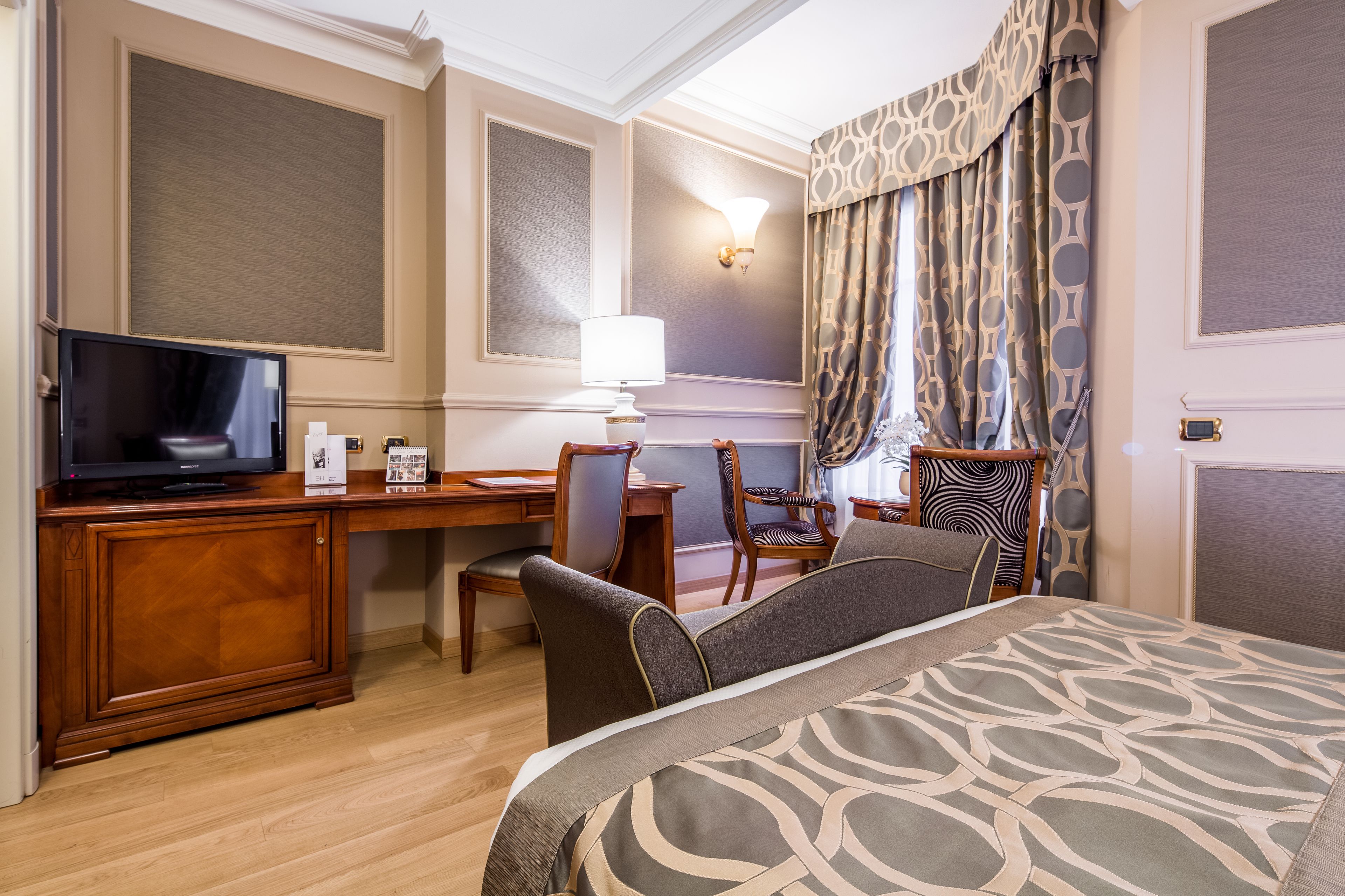 Habitación de hotel con cama, escritorio, televisión y una silla.