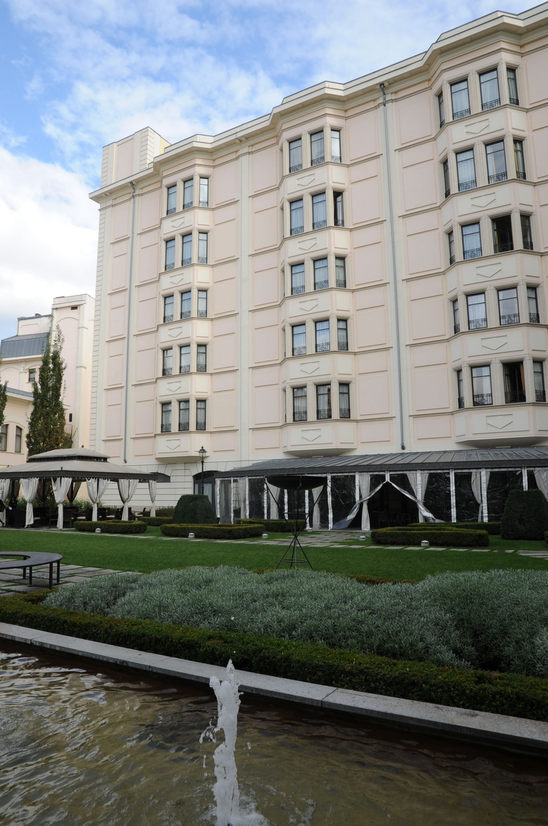 A large, multi-story hotel with a symmetrical facade, a courtyard with a fountain, and a well-maintained garden.