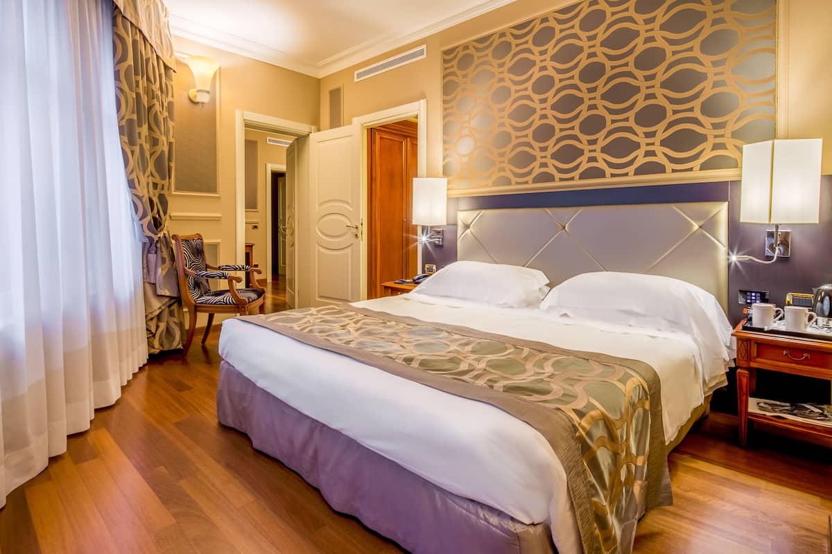 Une chambre d’hôtel avec un grand lit, une table de chevet, une chaise et un mur décoré d’un motif.