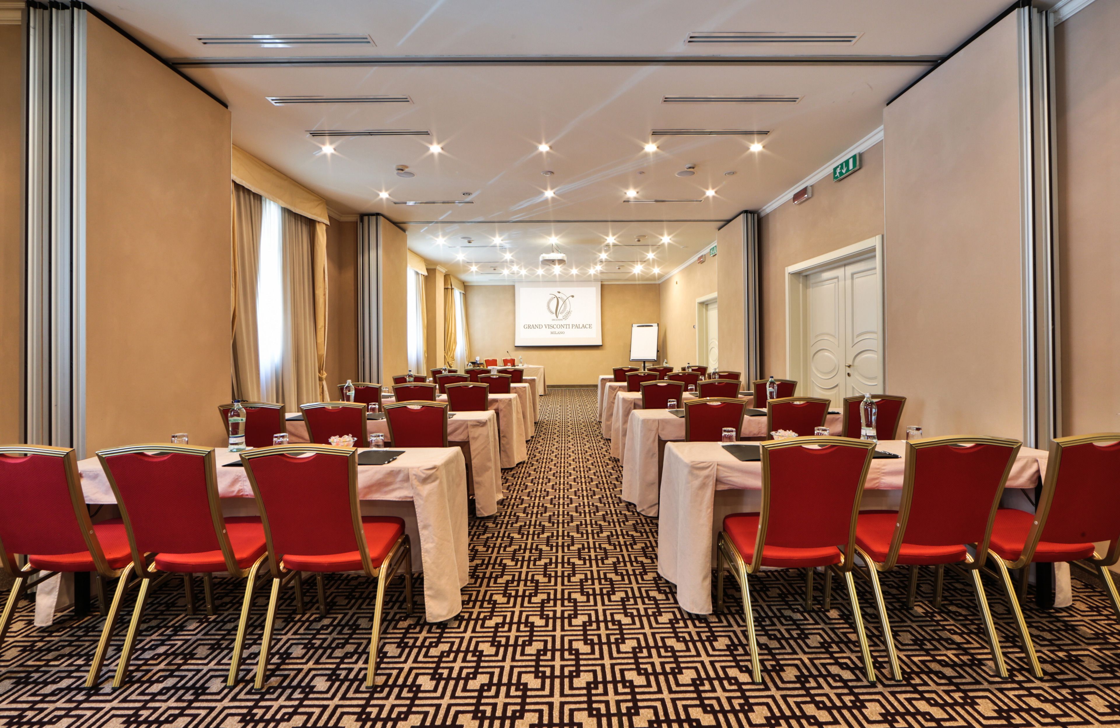 Ein Konferenzraum mit Tischen, Stühlen, einer Projektionsleinwand und einem gemusterten Teppich.