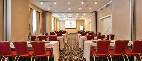 A conference room with tables and chairs, a projector screen, and a patterned carpet.