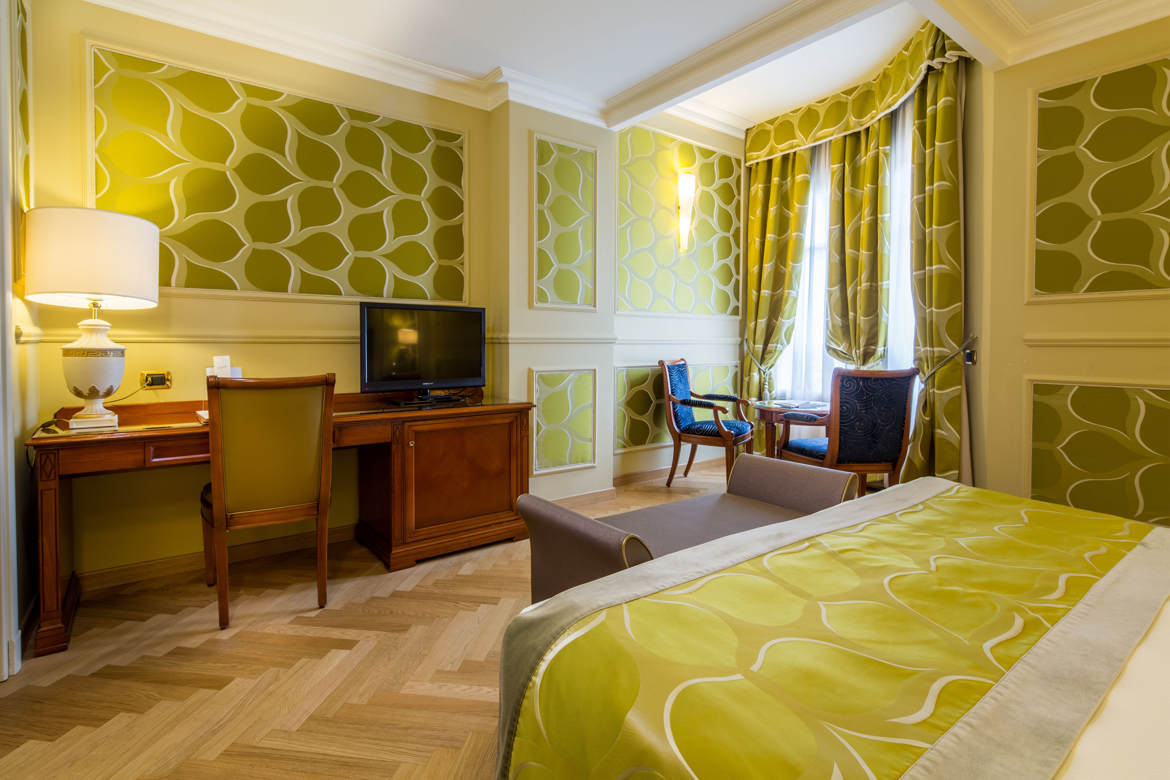 A hotel room with a bed, desk, TV, and seating area.