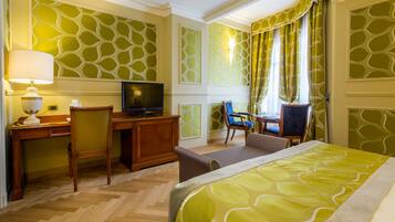 A hotel room with a bed, desk, TV, and seating area.