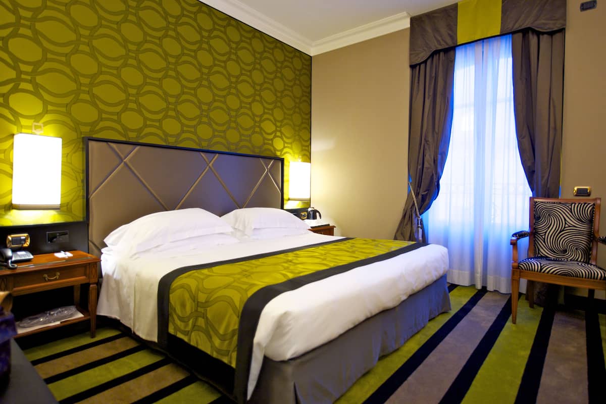 Une chambre d’hôtel avec un grand lit, deux tables de chevet, une chaise et une fenêtre avec des rideaux.