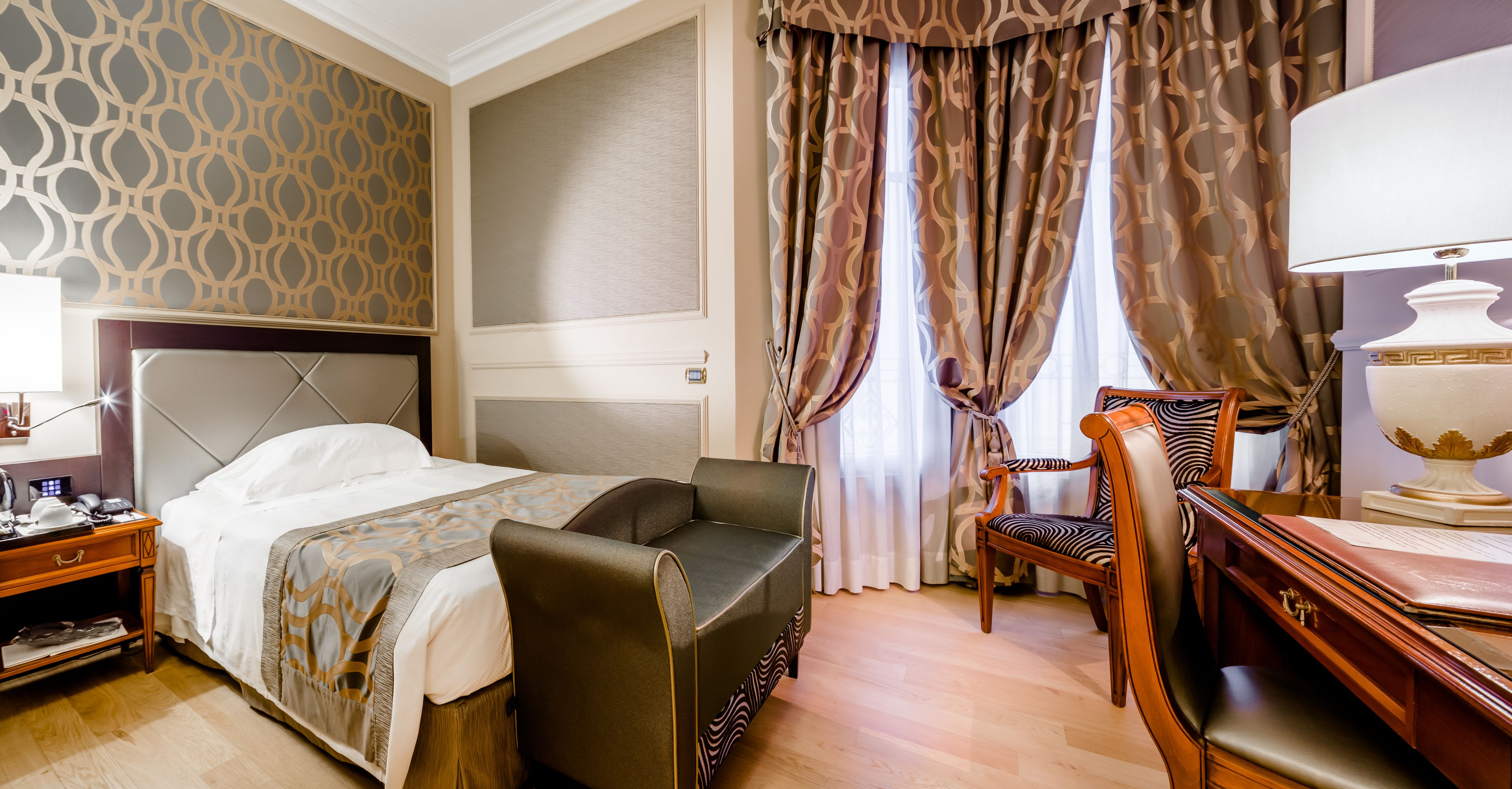 A hotel room with a bed, a desk, a chair, and a lamp.