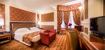 Een hotelkamer met een groot bed, een bureau, een televisie en een zithoek met een tafel en stoelen.