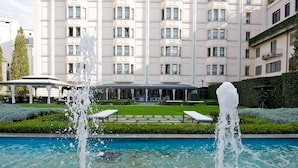 A pool with two water jets, a covered seating area, and a building with multiple balconies in the background. - Grand Visconti Palace (Milan)
