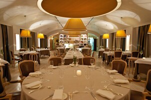 Een eetgedeelte met ronde tafels gedekt voor een maaltijd, met een centrale kaars en een boekenkast op de achtergrond.