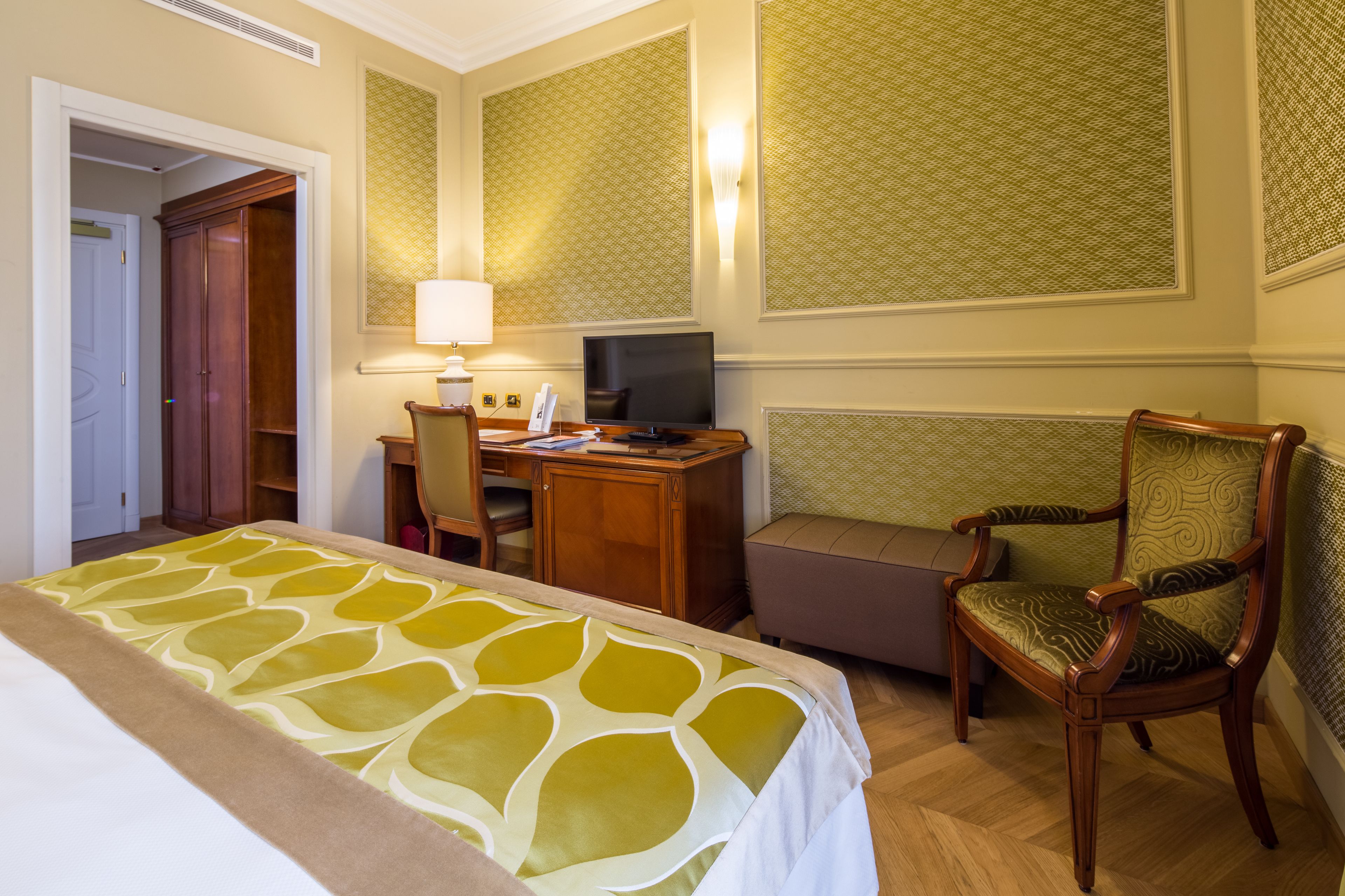 A hotel room with a bed, a desk with a computer, a chair, and a television.
