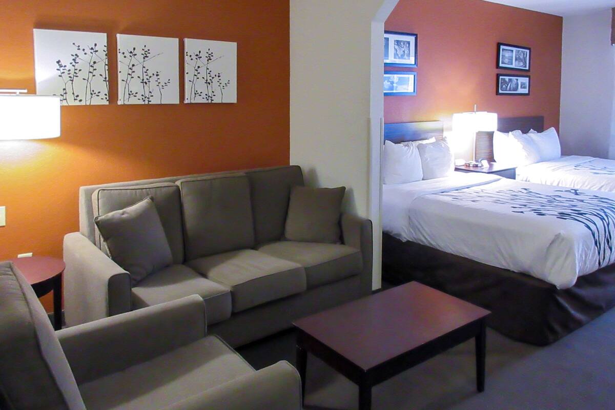 Una habitación de hotel con sofá, cama, mesita de noche y decoración en la pared.