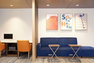 A modern office space with a desk, computer, and two chairs. There is a blue sofa with two side tables and artwork on the wall.