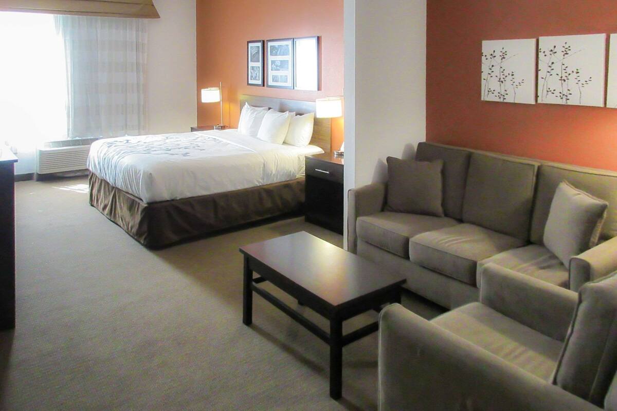 Una habitación de hotel con cama, sofá, mesa de centro y mesita de noche con lámparas.