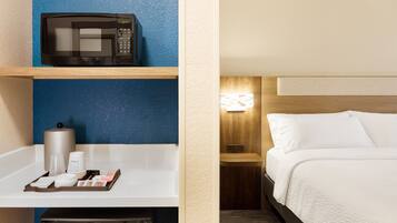 Une chambre d’hôtel équipée d’un four à micro-ondes posé sur une étagère, d’une poubelle, d’un plateau avec des articles de toilette et d’un lit avec du linge de lit blanc.