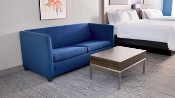 A hotel room with a blue sofa, a wooden coffee table, and a bed with white bedding.