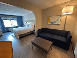 A hotel room with a bed, a sofa, a coffee table, and a painting on the wall.