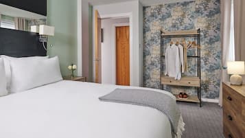 A hotel room with a large bed, a wooden wardrobe, a mirror, and a bedside table with a lamp.