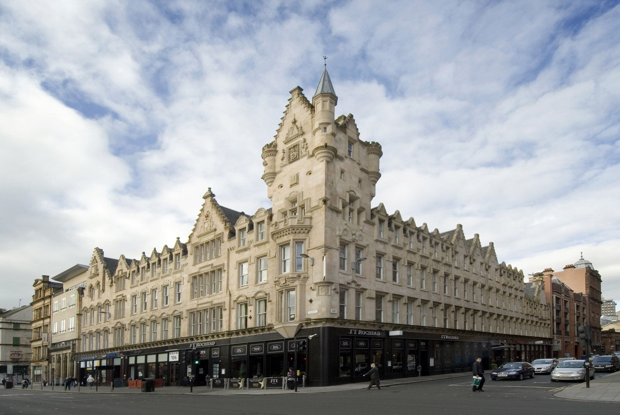 A large, historic building with a prominent tower and multiple storefronts on the ground floor.