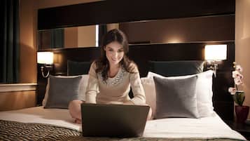 Habitación de hotel con cama, laptop y mesita de noche con lámpara.