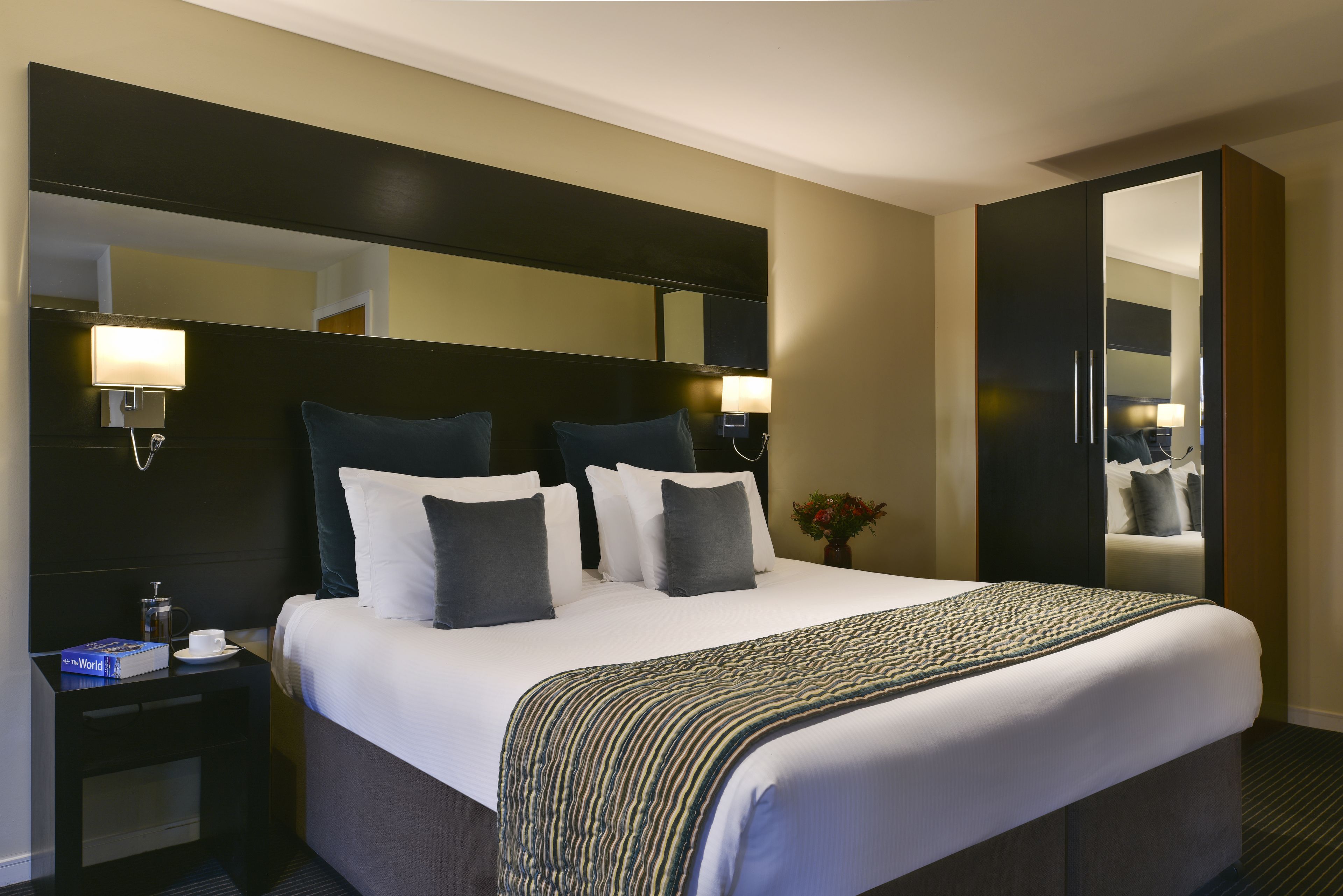 Une chambre d’hôtel avec un grand lit, une table de chevet avec une lampe, un miroir et une armoire.