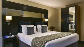 Une chambre d’hôtel avec un grand lit, une table de chevet avec une lampe, un miroir et une armoire.