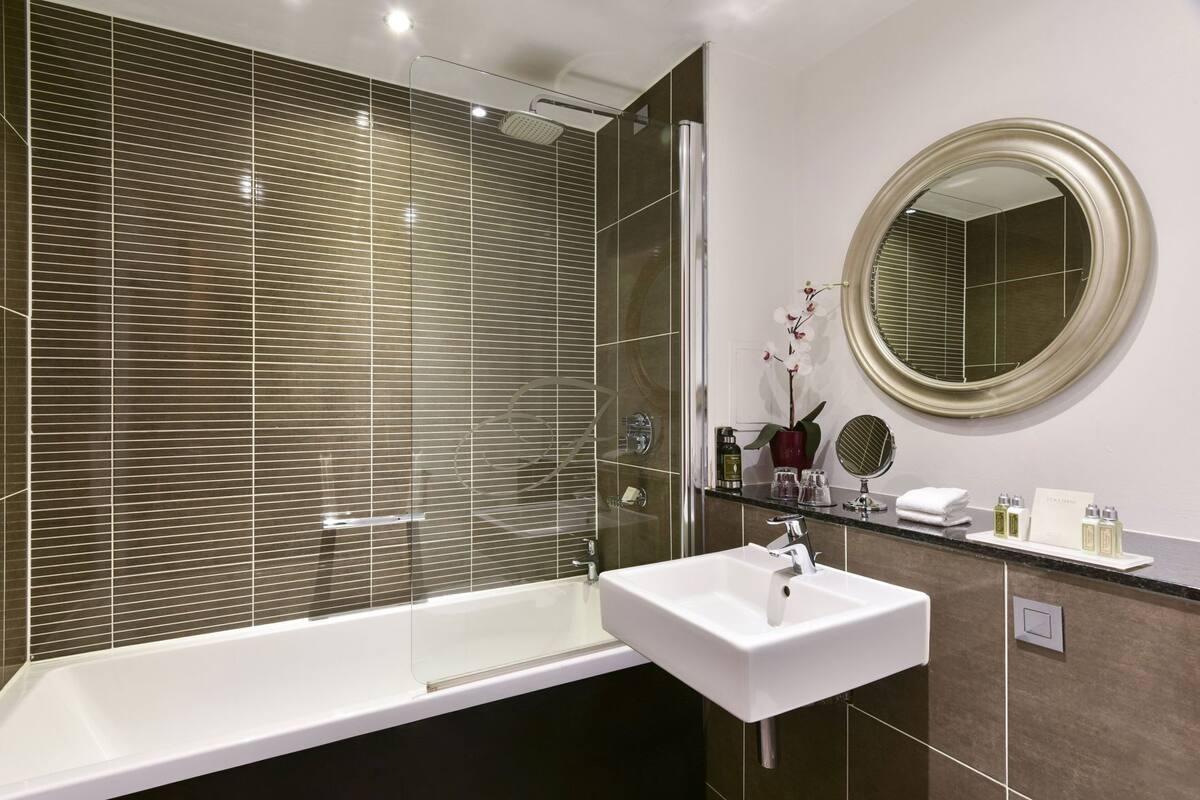 A modern bathroom with a large bathtub, a sink, a mirror, and a shower.